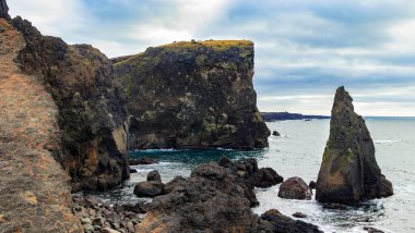 Arka planda uçurum olan kayalık bir kıyı şeridi. Su sakin ve gökyüzü bulutlu. Reykjanes Yarımadası