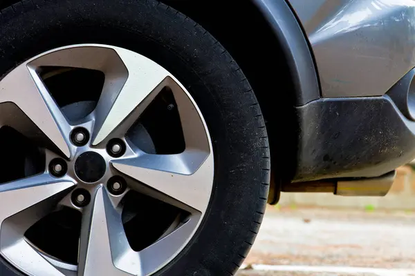Bir araba lastiği yakın planda gösterilir. Lastik siyah ve gümüşten. Lastik bir otoparkta.