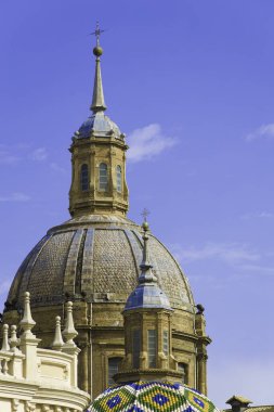 Tepesinde kubbe, tepesinde haç olan büyük bir bina. Bina mavi bir gökyüzü ile çevrilidir. El Pilar, Zaragoza Bazilikasının ayrıntıları