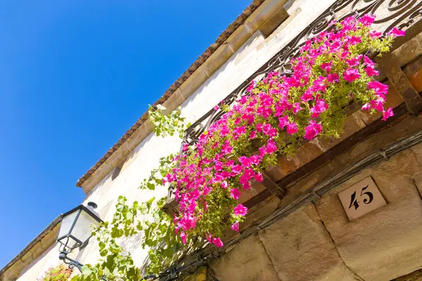 Üzerinde pembe çiçek aranjmanı ve 45 numara olan bir balkon. Çiçekler bir sepetin içinde ve balkon bir binaya bağlı.