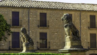 Two lion statues are sitting on a stone pedestal in front of a building. The statues are looking at the camera, and the building is brown and has a lot of windows clipart