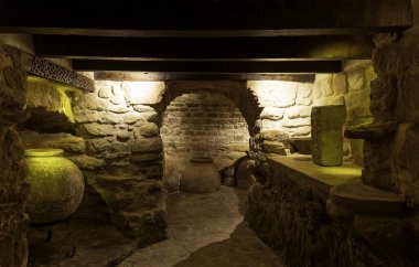 Eski ortaçağ tarzı bir depo. Taş bir duvarı ve yerde büyük bir vazosu olan eski bir oda. Oda loş bir şekilde aydınlatılmış, gizemli ve ürkütücü bir atmosfer yaratıyor.