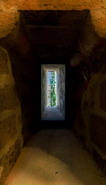 Ortasında küçük bir pencere olan dar, loş bir tünel. Pencere zar zor görülüyor ve tünel dar, bu da onu dar ve klostrofobik hissettiriyor.