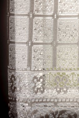 Kare ve dairelerden oluşan beyaz dantel bir perde. Perde pencerenin önünde asılı.