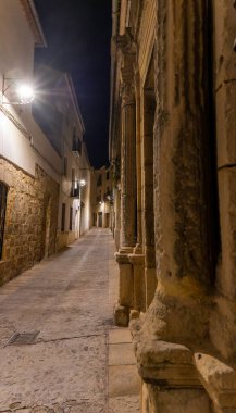 Baeza sokakları, İspanya, geceleri. Yan tarafında taş bir duvar olan dar bir sokak. Sokak lambaları sokakları aydınlatıyor ve binaların gölgeleri gizemli bir atmosfer yaratıyor.