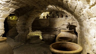 Bir sürü vazosu ve taş tavanı olan bir oda. Vazolar farklı boyutlarda ve şekillerde, ve bir derinlik ve boyut hissi yaratacak şekilde sıralanmış.