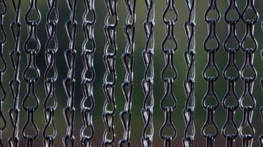 detail of a curtain made of several chains of small metal links swaying gently in the wind