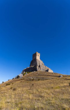 Atienza Kalesi, Guadalajara, İspanya. Açık mavi gökyüzü olan bir tepede yüksek bir bina var. Bina eski ve taş bir yapıya sahip.