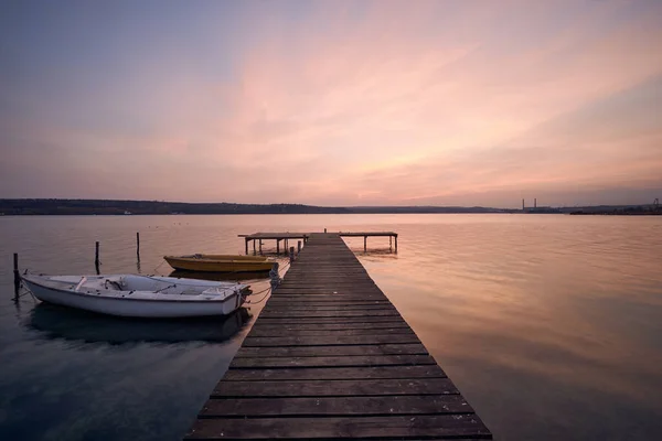 ブルガリアのヴァルナで日没時に湖に浮かぶ木製の桟橋と2隻のボートの風景写真 — ストック写真