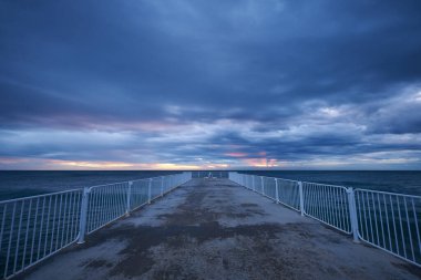 Fırtınalı karanlık denizin üzerinde dramatik gökyüzü olan terk edilmiş iskele gün doğumunda ya da günbatımında