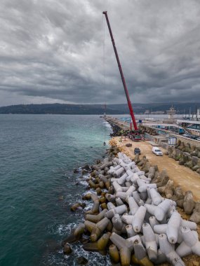 Dalgakıran inşaatının havadan görüntüsü. Denizde kaya yığınının üzerinde buldozer ve vinç, dikey atış
