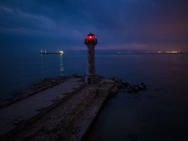 Deniz kıyısındaki deniz fenerinde gece kırmızı ışık altında gemilerin arka planında, Varna Bulgaristan.