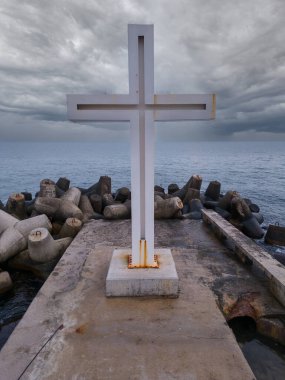 Denizde ya da okyanusta dramatik gökyüzü olan bir iskelede duran Hıristiyan haçı, hiç kimse