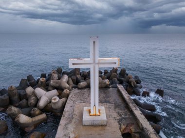 Denizde ya da okyanusta dramatik gökyüzü olan bir iskelede duran Hıristiyan haçı, hiç kimse