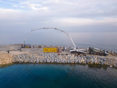 Ağır inşaat ekipmanları dalgakıran inşa ediyor. Denizde inşaat halindeki bir iskeleye beton dökmek. hava görünümü.