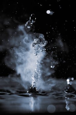 Kaynayan su, siyah arka planda buharla sıçrar.