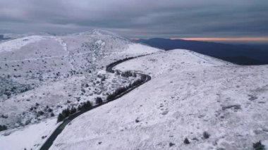 Kar, gün batımında dağları kaplamıştı. Öndeki hava manzaralı dolambaçlı bir yol vardı.