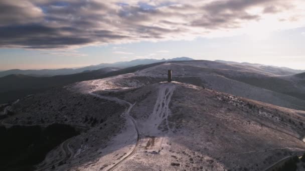 雪に覆われた山々と冬の朝にブルガリアのバルカン山脈の主尾根で自由の記念碑アーチの美しい空中トップビュー — ストック動画