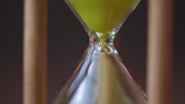 Sand running through the bulbs of an hourglass on a dark cork tree background close up.