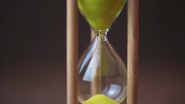 Sand running through the bulbs of an hourglass on a dark cork tree background close up.