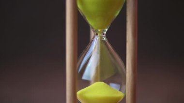 Sand running through the bulbs of an hourglass on a dark cork tree background close up.