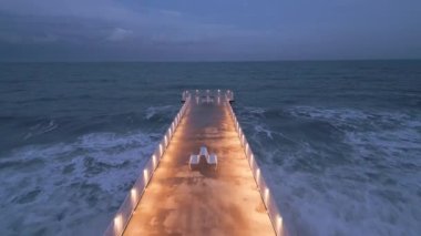 illuminated pier with dramatic sky over stormy dark sea at evening aerial view, Varna Bulgaria
