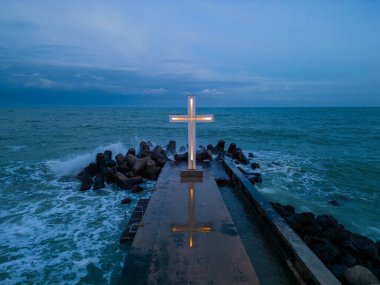 christian cross standing on pier in the stormy sea or ocean with dramatic sky at night