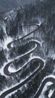 Aerial top down view of winter winding road in the dense forest, Transylvania, Romania.