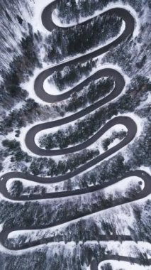 Aerial top down view of winter winding road in the dense forest, Transylvania, Romania.