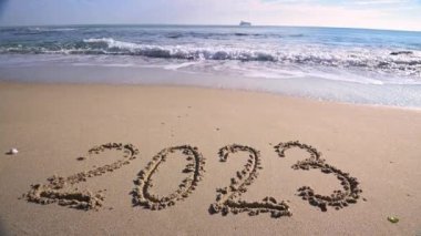 2023 year written on sandy beach ocean at sunny day