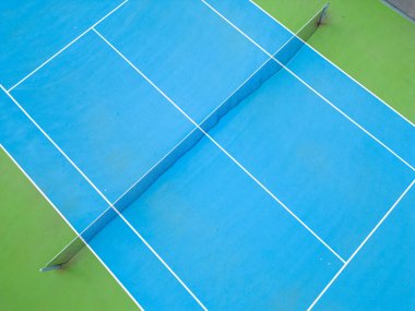 Boş bir eyalette sakin mavi-yeşil tenis kortunun havadan görünüşü, kortların iyi manikürlü yüzeyi ve onu işaretleyen çizgileri vurguluyor.