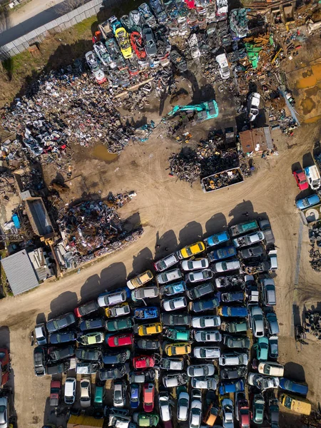 aerial view of a car dump, where a machine is seen separating old cars into scrap. The massive collection of abandoned cars and the heavy machinery used to process them are visible from above.