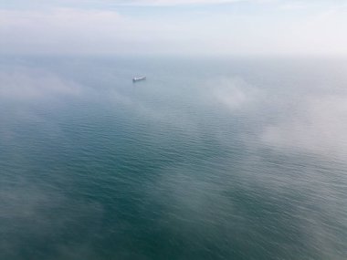 Sisli koşullarda seyreden gemilerin havadan görüntüsü. Bu tür bir görüş, gemilerin ölçeğini ve sisin yoğunluğunu göstererek, benzersiz ve potansiyel olarak ürkütücü bir perspektif sunabilir.