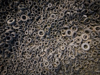 Kullanılmış araba lastikleriyle çevreleyen yeşil ağaçlar arasındaki katı kontrastın havadan görünüşü. Lastik damlalarının büyüklüğü çarpıcı, insanların olumsuz etkilerini vurguluyor.