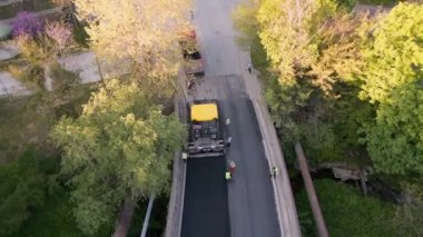Asfalt kaldırımlar, silindirler, makineler ve işçiler olarak yeni bir yol inşa etmenin havadan görüntüsü hayati bir ulaşım bağlantısı oluşturmak için bir araya geliyor. Etkileyici koordinasyon ve takım çalışmasına tanık olun.