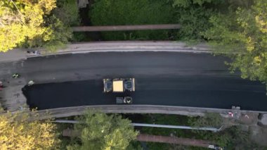 Asfalt kaldırımlar, silindirler, makineler ve işçiler olarak yeni bir yol inşa etmenin havadan görüntüsü hayati bir ulaşım bağlantısı oluşturmak için bir araya geliyor. Etkileyici koordinasyon ve takım çalışmasına tanık olun.