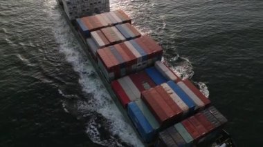 Bir konteynır gemisinin havadan görünüşü denizde yelken açar. Devasa gövdesi, kargoyu dünyanın öbür ucuna taşırken suyu keserek geçer. Gemi sonsuz dalgalarla çevrili.