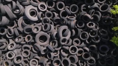 Kullanılmış araba lastikleriyle çevreleyen yeşil ağaçlar arasındaki katı kontrastın havadan görünüşü. Lastik damlalarının büyüklüğü çarpıcı, insanların olumsuz etkilerini vurguluyor.
