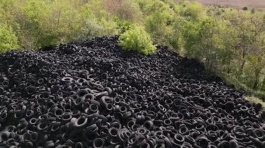 Kullanılmış araba lastikleriyle çevreleyen yeşil ağaçlar arasındaki katı kontrastın havadan görünüşü. Lastik damlalarının büyüklüğü çarpıcı, insanların olumsuz etkilerini vurguluyor.