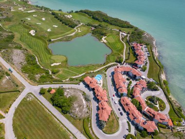 Alttaki golf sahasının havadan görünüşü, yemyeşil çayırları nefes kesen kıyı manzarasını tamamlıyor. Resmedilmeye değer manzaralar arasında, lüks villalar stratejik olarak yerleştirilmiş, zarafet ve manzaranın kusursuz bir birleşimi sunuluyor.