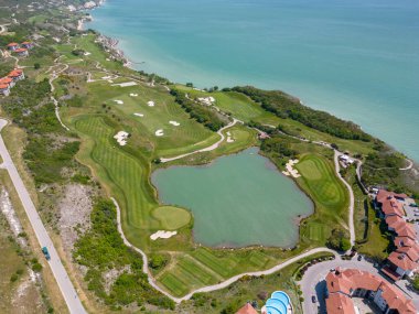 Alttaki golf sahasının havadan görünüşü, yemyeşil çayırları nefes kesen kıyı manzarasını tamamlıyor. Resmedilmeye değer manzaralar arasında, lüks villalar stratejik olarak yerleştirilmiş, zarafet ve manzaranın kusursuz bir birleşimi sunuluyor.