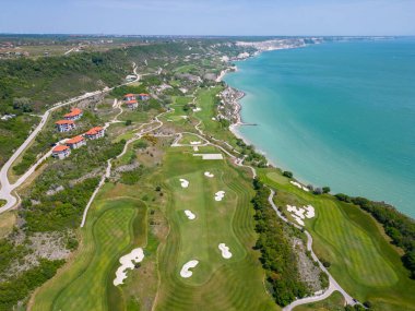 Alttaki golf sahasının havadan görünüşü, yemyeşil çayırları nefes kesen kıyı manzarasını tamamlıyor. Resmedilmeye değer manzaralar arasında, lüks villalar stratejik olarak yerleştirilmiş, zarafet ve manzaranın kusursuz bir birleşimi sunuluyor.