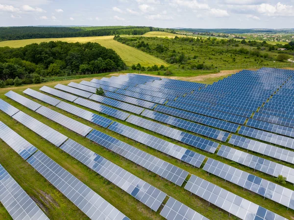 Amidst a lush meadow and forest, solar panels stand tall, harnessing the suns energy. Their gleaming surfaces reflect the vibrant sky, creating a mesmerizing sight. Captured from a drones