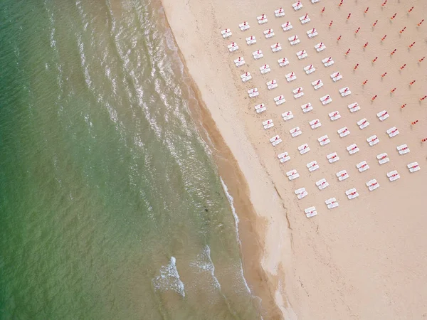 stock image A sandy beach stretches along the seaside, adorned with empty sun loungers. From an aerial perspective, the tranquil scene unfolds, with the azure sea meeting the golden shoreline. The vacant sunbeds