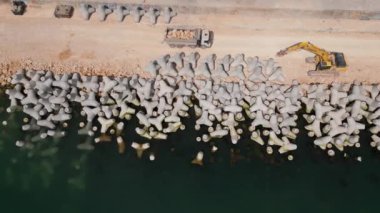 Bir kazı ustalıkla denizde bir rıhtım ya da dalgakıran inşa eder. Güçlü kolu kıyıdan uzanarak dalgaların arasında dirençli bir yapı oluşturur. Havadan üst görünüm