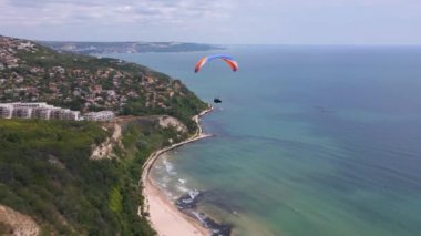 Bulgaristan 'ın Albena tatil beldesinin nefes kesici manzarasıyla deniz ve orman üzerinde süzülen bir paraglider unutulmaz bir deneyim yaratıyor. İHA uçuş videosu.