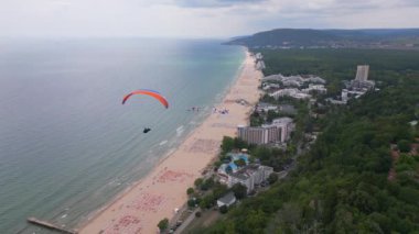 Bulgaristan 'ın Albena tatil beldesinin nefes kesici manzarasıyla deniz ve orman üzerinde süzülen bir paraglider unutulmaz bir deneyim yaratıyor. İHA uçuş videosu.