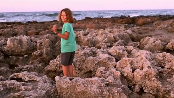 Девятилетний Мальчик Длинными Светлыми Волосами Ловко Прыгает Вдоль Скалистого Моря — стоковое видео