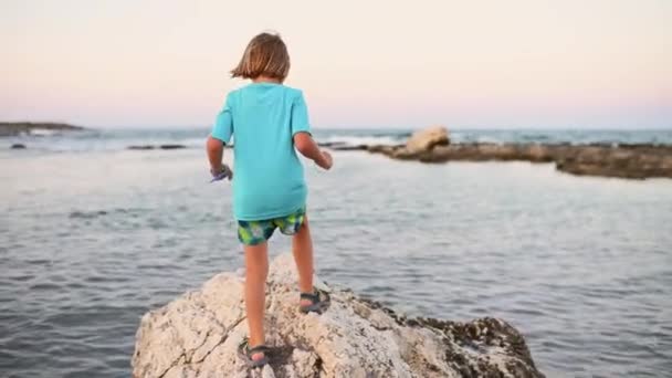 一个5岁的男孩 一头长长的 浅色的头发 敏捷地跃过岩石海岸 探索着每一个角落 — 图库视频影像