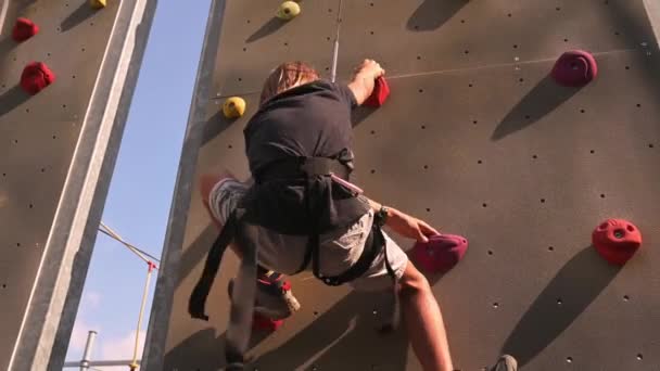 一个长发男孩在户外熟练地爬上了攀岩墙 掌握了自己的身高和极限 夏季时间 — 图库视频影像